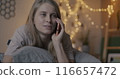 Pretty young lady chatting on mobile phone discussing news smiling lying in bed in illuminated bedroom in evening. People and cellphone communication concept. 116657472