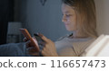 Happy young woman using smartphone and holding credit card paying in online store shopping sitting in bed in apartment in evening. E-commerce and money concept. 116657473