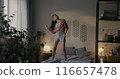 Young Asian woman dancing on bed wearing pajamas listening to music enjoying free time in bedroom in morning. Youth and entertainment concept. 116657478