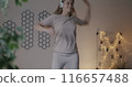 Happy young woman dancing on bed listening to music with headphones having fun in bedroom in evening. Leisure activity and youth lifestyle concept. 116657488