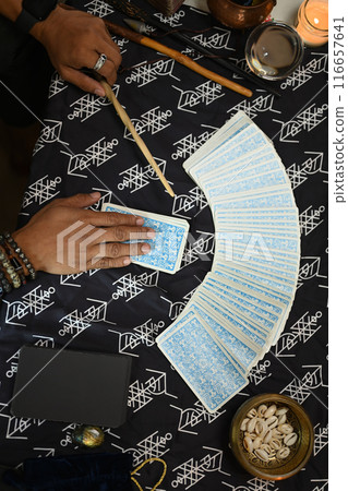 Overhead shot of fortune teller spreading Tarot cards laid out on a table covered with mystical cloth Overhead shot of fortune teller spreading Tarot cards laid out on a table covered with mystical cloth 116657641