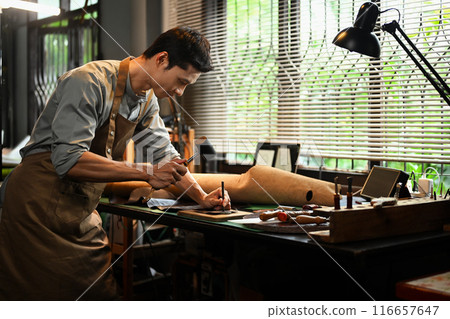 Male artisan holding a tool and a hammer to puncture or shape the leather on a workbench Male artisan holding a tool and a hammer to puncture or shape the leather on a workbench 116657647