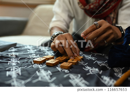 Man arranging wooden runes on a table covered with a mystical cloth. Forecasting and divination concept Man arranging wooden runes on a table covered with a mystical cloth. Forecasting and divination concept 116657653