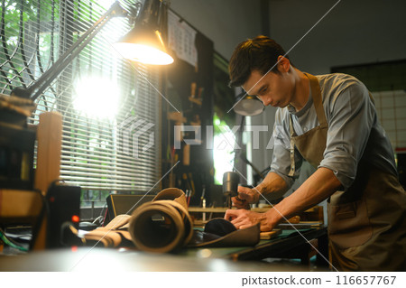 Focused craftsman intently working on a leather project in his local workshop 116657767