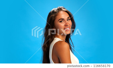 Portrait of beautiful, young woman looking at camera over shoulder against blue studio background. Trendy colors. 116658170