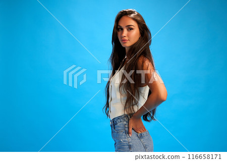 Side view portrait of young woman in casual attire looking at camera against blue studio background. Trendy colors. 116658171