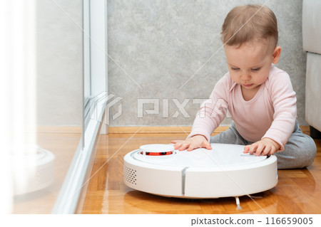 A baby tries to push a working robot vacuum cleaner. Concept of interaction with smart devices A baby tries to push a working robot vacuum cleaner. Concept of interaction with smart devices 116659005