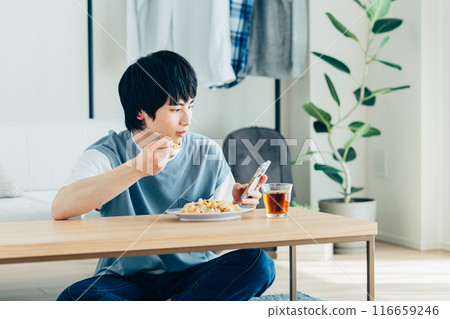 A young man eating fried rice and looking at his smartphone 116659246