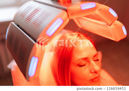 Closeup head of blonde female with closed eyes having LED red light hair photodynamic therapy during hair treatment in clinic. Young woman patient having non-invasive type of phototherapy. 116659451