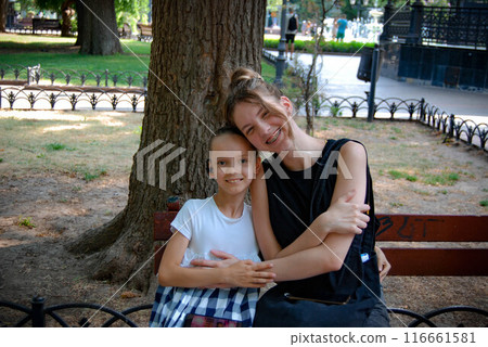 Relaxing on a bench in the park. A joyful meeting of two sisters in the park. Relaxing on a bench in the park. A joyful meeting of two sisters in the park. 116661581
