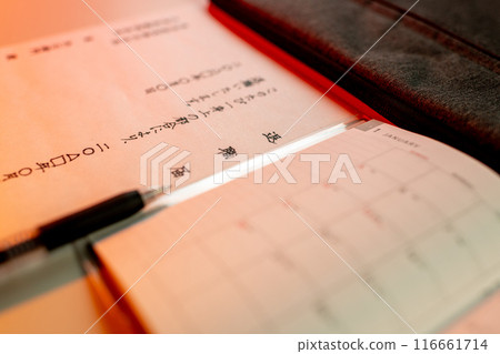 A handwritten resignation letter illuminated by red light, a gel ink black pen, and a new schedule book 116661714