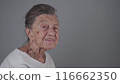 Senior woman 90 years old smiles, laughs and shows a denture on a gray background. Elderly female with deep wrinkles and gray hair happy in a good mood studio portrait looking at camera 116662350