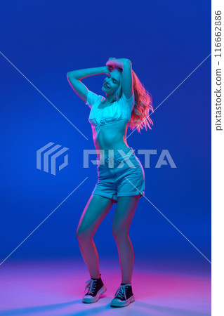 Full-body portrait of young woman, student wearing summer outfit dancing in motion in neon light against gradient studio background. Trends. Full-body portrait of young woman, student wearing summer outfit dancing in motion in neon light against gradient studio background. Trends. 116662886