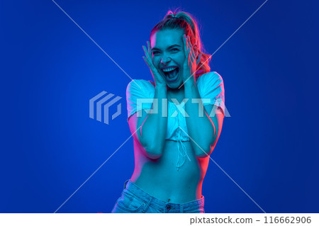 Excited young woman holding hands near face and shouting out of shock in neon light against gradient studio background. Trends. 116662906