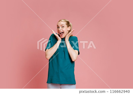 Excited young woman holding hands near face and shouting out of surprise against pastel pink studio background. 116662940