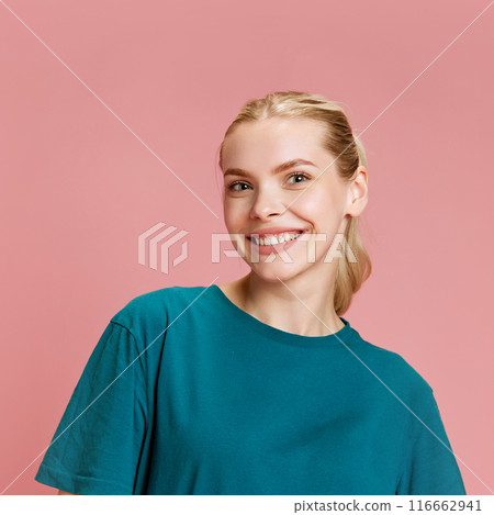 Portrait of young attractive woman looking at camera with wide smile against pastel pink studio background. Portrait of young attractive woman looking at camera with wide smile against pastel pink studio background. 116662941
