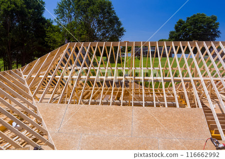 Installation of wooden roofing truss frame while house is being constructed roof Installation of wooden roofing truss frame while house is being constructed roof 116662992