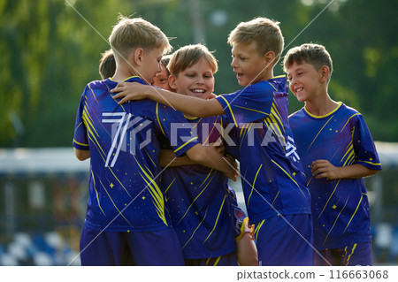 Happy smiling children, boys in blue sportswear hugging, smiling and celebrating successful winning soccer game. Happy smiling children, boys in blue sportswear hugging, smiling and celebrating successful winning soccer game. 116663068