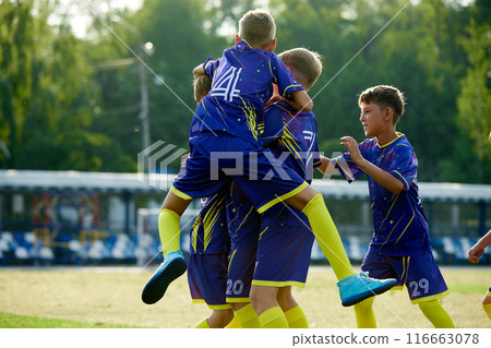 Dynamic moment of victory. Boys, friends in blue uniform, soccer players in motion, jumping and hugging, celebrating winning game. 116663078