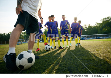 Focus on male legs and soccer ball, coach showing boys how to dribble ball through field. Outdoor soccer game training Focus on male legs and soccer ball, coach showing boys how to dribble ball through field. Outdoor soccer game training 116663201