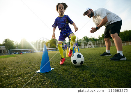 Male sport coach guiding young player through dribbling drill, encouraging and commentating. Focus and concentration Male sport coach guiding young player through dribbling drill, encouraging and commentating. Focus and concentration 116663275