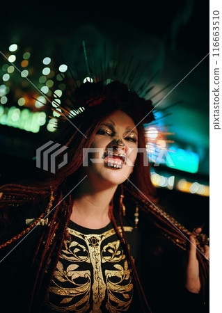 Girl with skeleton makeup at a Halloween party make grimaces and looks at camera. Celebration in a nightclub. Female in creepy costume of Mexican goddess of death. All Saints' Night. 116663510