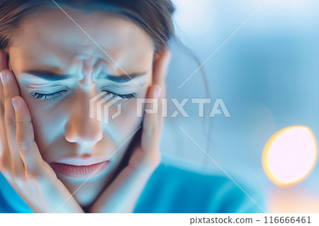A woman looks down with a sad expression and her hands on her face 116666461