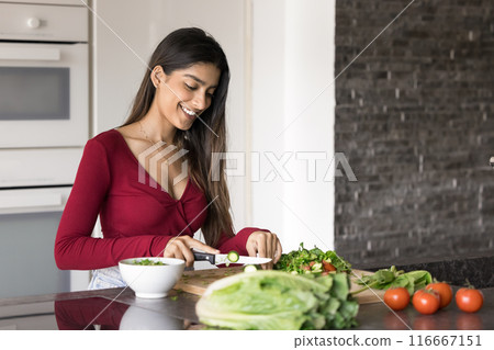 Happy beautiful young adult Indian girl cooking salad in kitchen Happy beautiful young adult Indian girl cooking salad in kitchen 116667151