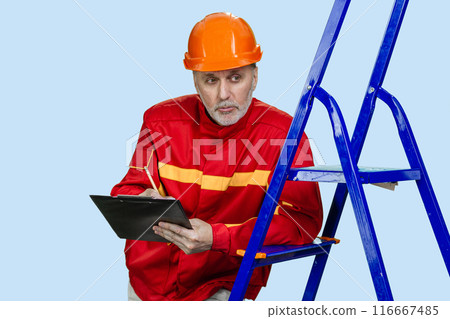 Senior aged contruction worker with clipboard and pencil. Isolated on blue. 116667485