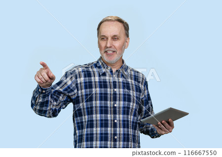 Smiling senior man holding tablet pc device and pointing at something. Isolated on blue. Smiling senior man holding tablet pc device and pointing at something. Isolated on blue. 116667550