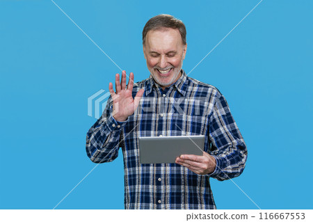 Portrait of happy mature man waving his hand to someone online. Isolated on vivid blue. Portrait of happy mature man waving his hand to someone online. Isolated on vivid blue. 116667553