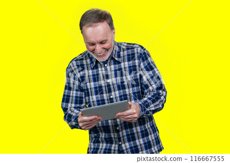 Aged mature man is looking at digital tablet and laughing. Isolated on yellow. 116667555