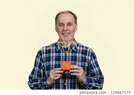 Portrait of smiling handsome senior man is holding a red gift box in both hands. Isolated on white. Portrait of smiling handsome senior man is holding a red gift box in both hands. Isolated on white. 116667575