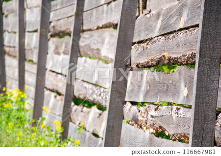 A close-up image showcasing a rustic wooden fence constructed with horizontal planks and sturdy black posts. The wood is weathered and aged, with visible signs of time and exposure to the elements 116667981