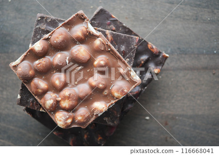 A stack of delicious gourmet chocolate bars topped with nuts on a wooden surface 116668041