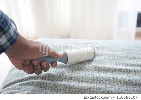 using an adhesive roller to remove lint and fluff from a bed . using an adhesive roller to remove lint and fluff from a bed . 116668107
