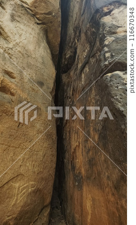 A narrow crack separates two large sandstone cliff faces. Vertical mobile photo. sstkvertical 116670348