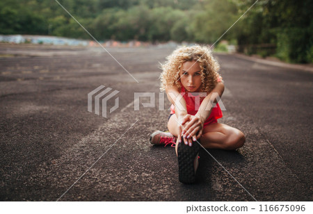 A young curly blonde of athletic build performs a warm-up before training at the stadium. Outdoor sports 116675096