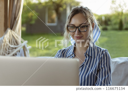 glasses for vision. Elegant freelance girl works at a laptop outside the house glasses for vision. Elegant freelance girl works at a laptop outside the house 116675134