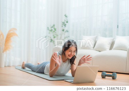 Young Asian woman lying on the floor on yoga mat in front of laptop and training at hom 116676123