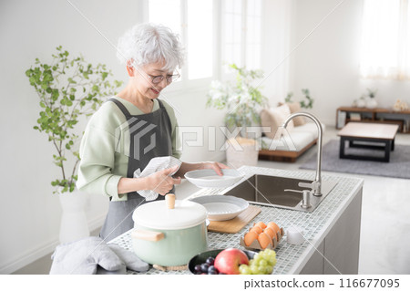 Senior woman doing housework and cooking, wiping dishes in island kitchen Senior woman doing housework and cooking, wiping dishes in island kitchen 116677095
