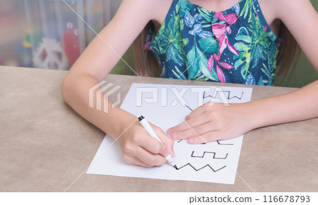 Schoolgirl draws lines with black pen. Writing practice. Childhood and activities at home. 116678793