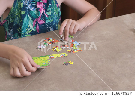 Young teenage girl putting together puzzle on table at home. Toys and activiti for children. Developmental activities at home.  116678837