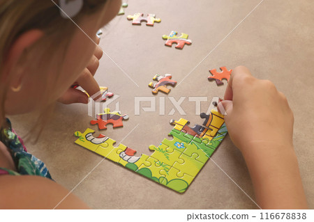 Young teenage girl putting together puzzle on table at home. Toys and activiti for children. Developmental activities at home. Young teenage girl putting together puzzle on table at home. Toys and activiti for children. Developmental activities at home. 116678838