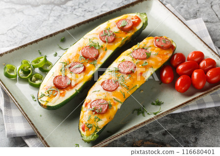 Summer appetizer of zucchini stuffed and baked with cheddar and mozzarella cheese, sausages and tomato sauce close-up in a plate. Horizontal 116680401