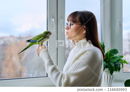 Middle aged woman and parrot together at home, near winter window 116680993