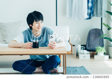 A young man looking at his smartphone in the living room 116683885