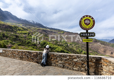 Tourist at viewing platform overseeing Danba Jiaju Tibetan Village with signpost message in Chinese translated to be Danba Jiaju, China Most beautiful Village Tourist at viewing platform overseeing Danba Jiaju Tibetan Village with signpost message in Chinese translated to be Danba Jiaju, China Most beautiful Village 116686710