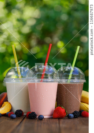 set of different flavor milkshakes or smoothie in disposable plastic glasses on wooden table outdoors 116687973