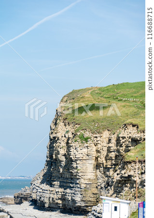 Steep cliffs and rocky coastline with exposed geological formations on the coastline, in the suburbs of South Wales Steep cliffs and rocky coastline with exposed geological formations on the coastline, in the suburbs of South Wales 116688715